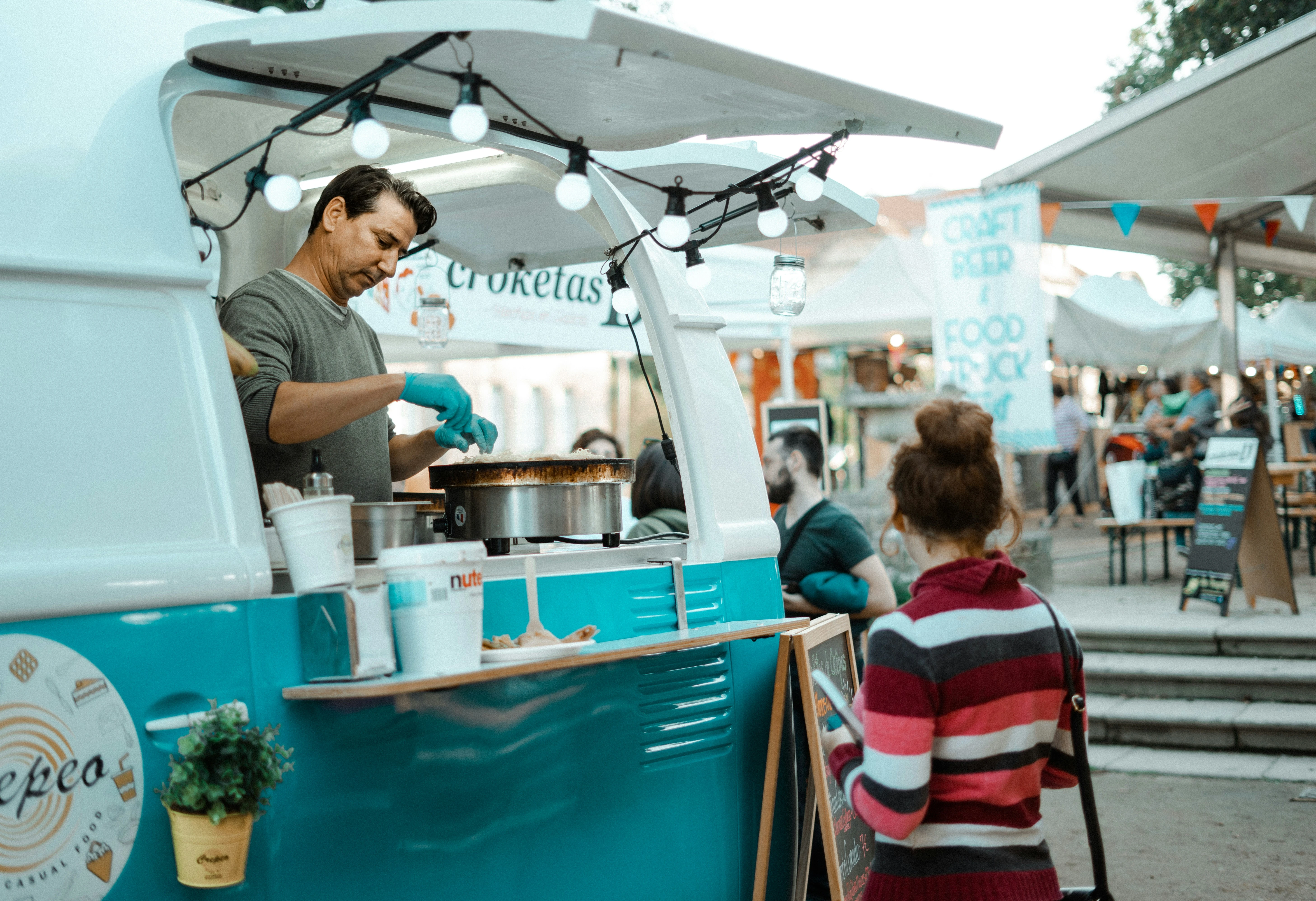 A person cooking a crepe in a foodtruck and a person waiting for it